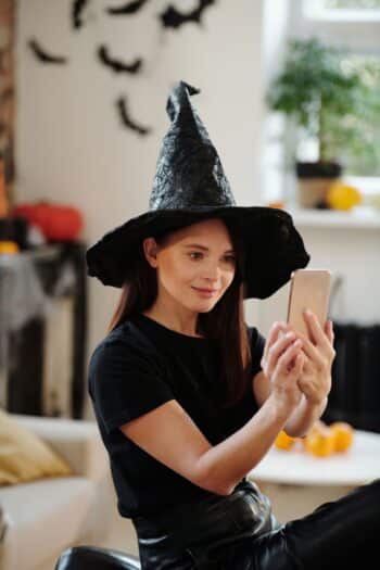 Woman in a black top and witch hat taking a Halloween selfie