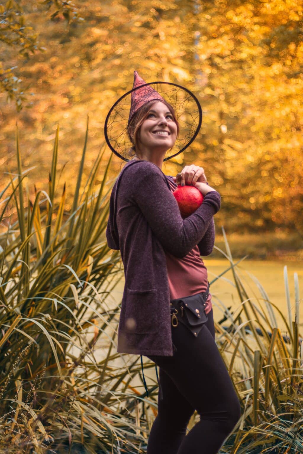 Woman wearing a witch hat and holding a pumpkin outdoors