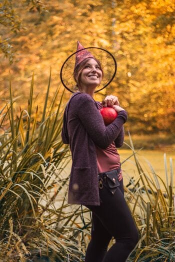 Woman wearing a witch hat and holding a pumpkin outdoors