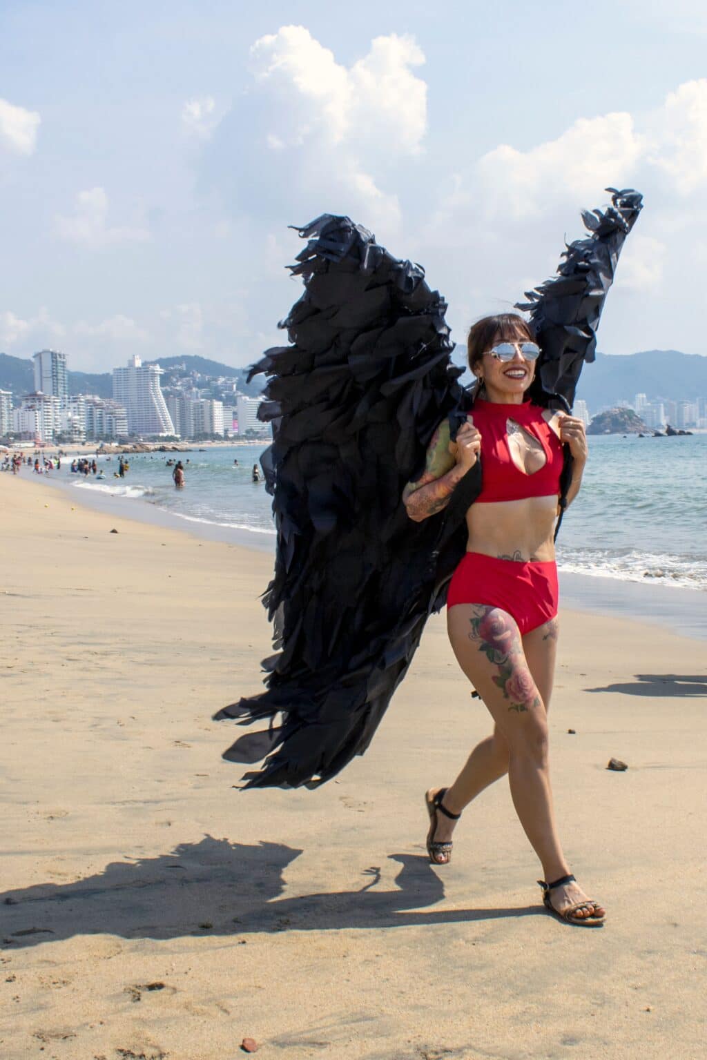 Woman wearing a lightweight red costume with black wings on a sunny beach