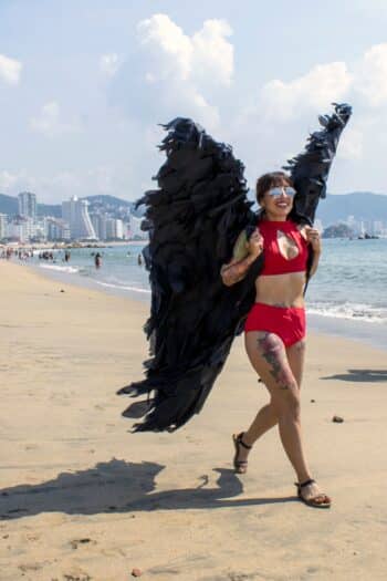 Woman wearing a lightweight red costume with black wings on a sunny beach