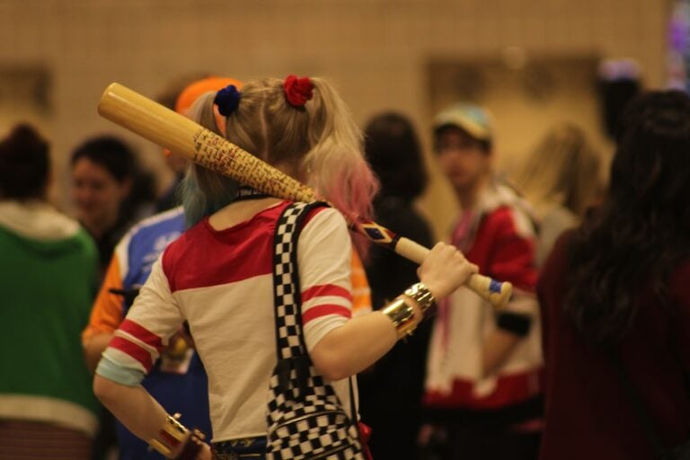 Cosplayer dressed as Harley Quinn carrying a prop bat at a comic convention
