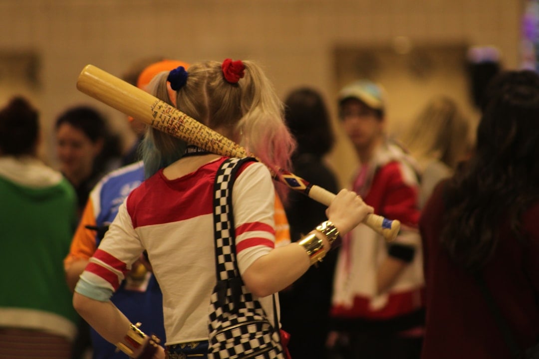 Cosplayer dressed as Harley Quinn carrying a prop bat at a comic convention