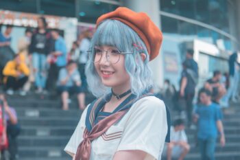 Cosplayer wearing a short blue wig, glasses and an orange beret