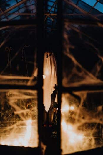 A ghost costume seen through a window decorated with Halloween cobwebs